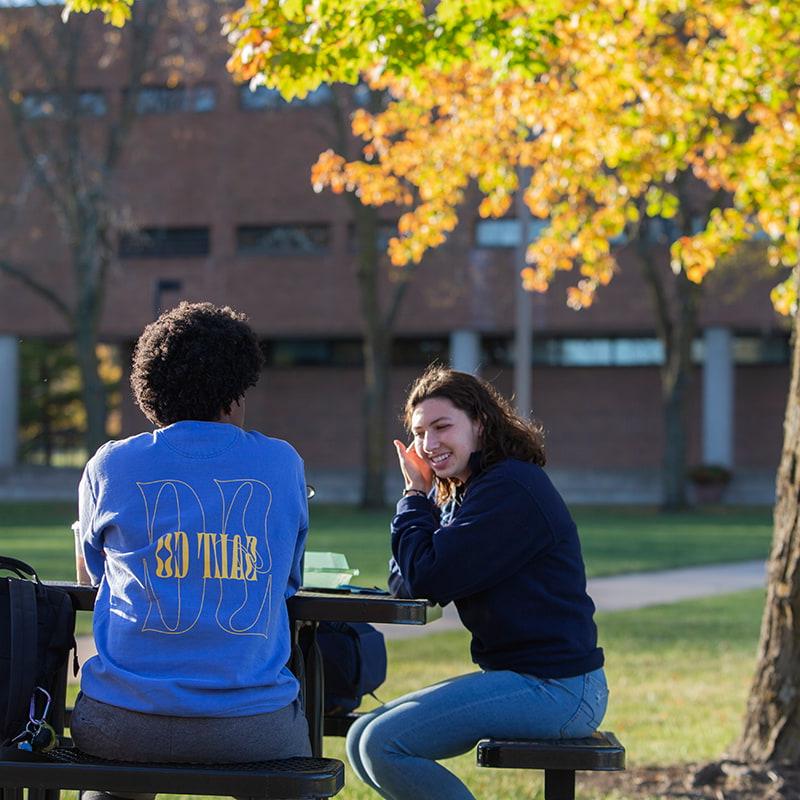 两个威尼斯人网上娱乐的学生坐在校园外的长凳上聊天