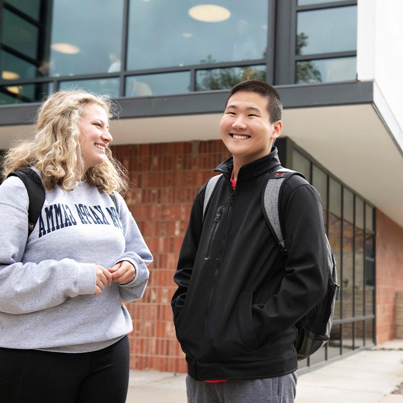 Two Drake University students standing next to each other smiling while standing outside of a dining hall on campus